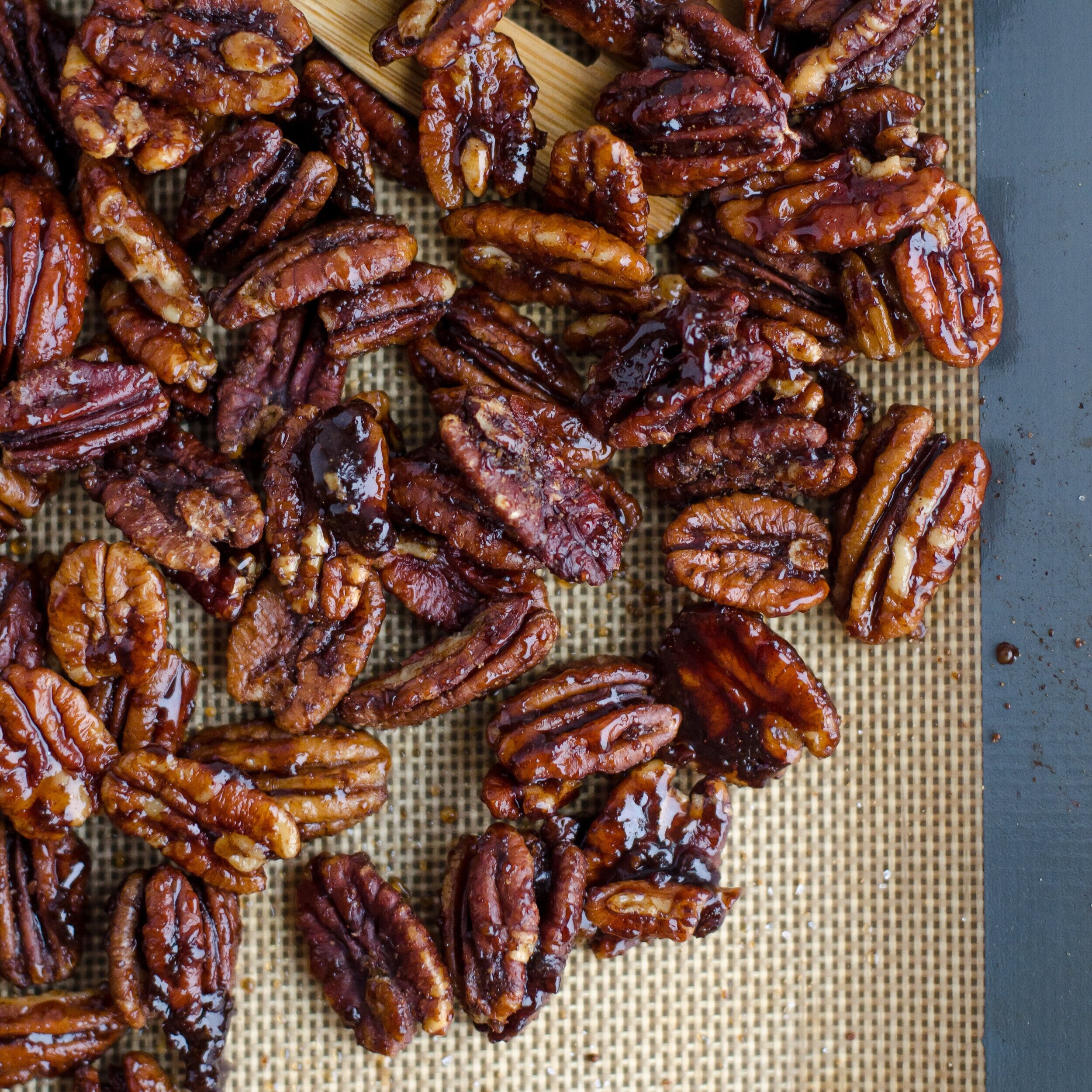 Sweet and crunchy caramelized pecans spread out on a baking mat, showcasing their glossy finish and rich brown hues, perfect for snacking or adding to desserts.